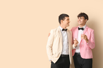 Married gay couple with glasses of champagne on beige background