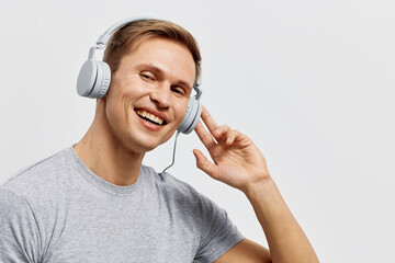 Smiling man wearing casual gray t-shirt listening to headphones looking at camera isolated on white...