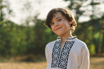 A young boy smiles confidently while standing in a sunlit field, wearing a traditional embroidered...