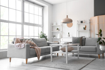 Interior of light living room with grey sofas and coffee table near big window
