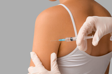 Dermatologist taking puncture from young woman's mole on light background, closeup