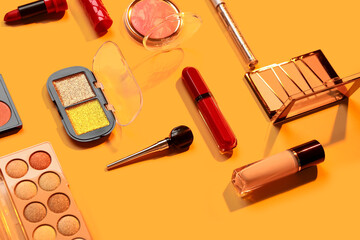 Beautiful palettes of eyeshadows and different decorative cosmetics on orange background