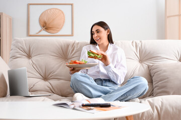 Young woman with tasty sandwiches and laptop at home