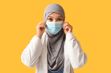 Female Muslim doctor in hijab and face mask on orange background. World Hijab Day concept