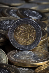 Moneda mexicana de 5 pesos sobre un fondo obscuro lleno de monedas.

Mexican 5 peso coin on a dark background filled with coins.