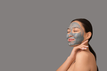 Young woman with clay mask on her face against grey background