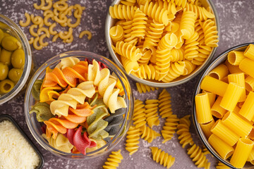 Bowls with different uncooked pasta on grey grunge background, closeup
