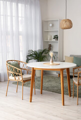 Stylish interior of spacious living room with table, armchairs, houseplants and shelving unit