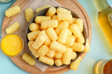 Bowl with tasty salty corn sticks and sauce on blue background, closeup