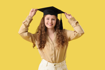 Happy female student in graduation hat on yellow background