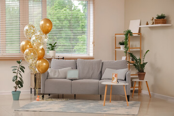 Beautiful golden air balloons with sofa and coffee table near beige wall at home