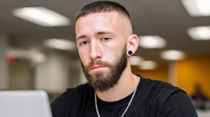 Obraz premium Young man with short hair and beard wearing a black shirt and silver chain