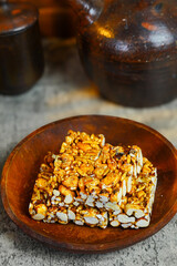 A plate of sweet Brondong, an Indonesian puffed rice snack, is placed on a rough surface next to a traditional earthenware jug in a rustic, low-key setting.