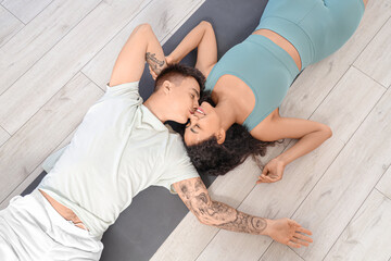 Young couple kissing while lying on yoga mat at home