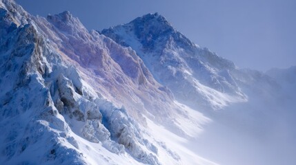 Fototapeta premium Jagged snowy mountain peaks shrouded in mist under a clear blue sky winter
