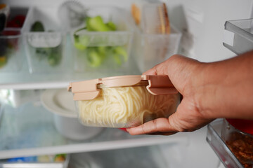 Hand holding a container of pasta in a refrigerator