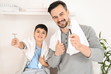 Happy father and his little son holding razors with towels in bathroom