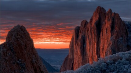 Dramatic mountain peaks bathed in fiery sunset light with a dark cloudy sky
