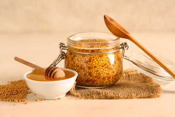 Jar with Dijon mustard and bowl of honey on beige background