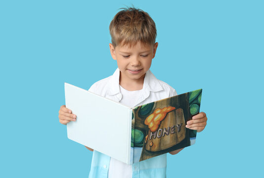 Portrait of cute little boy reading book on blue background