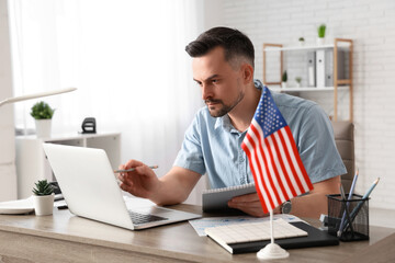 Handsome young man with laptop and flag of USA writing in notebook at office