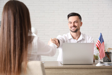 Happy businessman with flag of USA shaking hands with female colleague in office