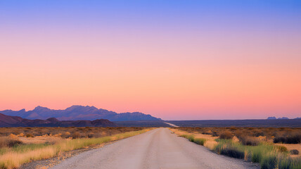 Fototapeta premium Long dusty desert road leading to rugged silhouetted mountains under a vibrant sunrise sky with soft warm lighting and sparse arid vegetation