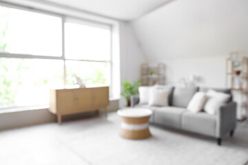 Blurred view of living room with grey sofa, table and shelf units