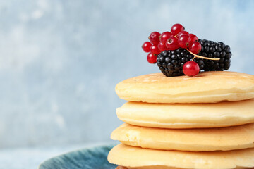 Plate of sweet pancakes with fresh blackberries and red currants on light blue background, closeup