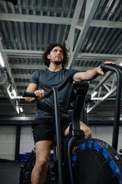 Vertical low angle view of Caucasian man in sportswear using cycling training machine in gym, copy space
