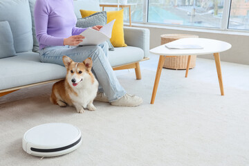 Cute Welsh Corgi dog with owner and robot vacuum cleaner in room
