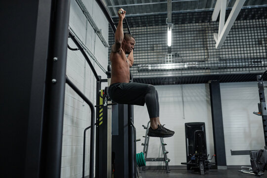 Side view wide shot of young African American man with muscular body doing pull-ups on bar in modern gym