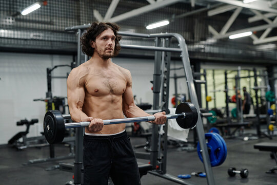 Young Caucasian man with muscular body doing workout topless in gym