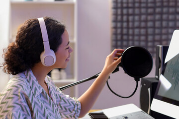 Young African-American woman with headphones and microphone in recording studio