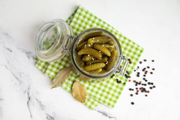 Jar with tasty pickled cucumbers, peppercorns and bay leaves on white background