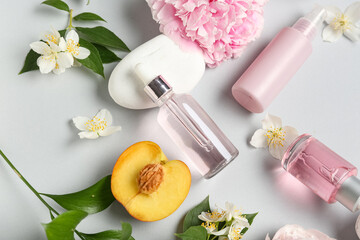 Natural cosmetic products with flowers, peach and spa stones on grey background