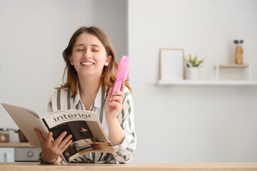 Young woman with mini fan reading magazine in kitchen