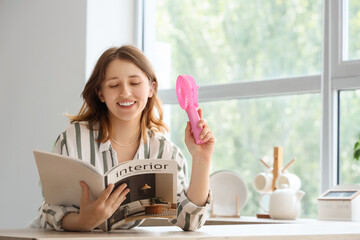 Young woman with mini fan reading magazine in kitchen