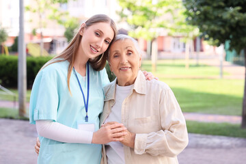 Fototapeta premium Smiling young caregiver and senior woman embracing outdoors, healthcare and elder care support