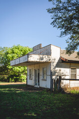 A derelict building with a prominent cantilevered awning stands in a grassy field under a clear...