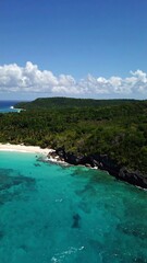 Fototapeta premium Aerial view of a tropical beach with turquoise water, lush green vegetation, and a rocky shoreline