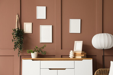 Chest of drawers with houseplant, vase and books near brown wall in living room, closeup