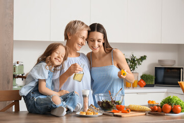 Little girl with her mother and granny making vegetable salad at table in kitchen