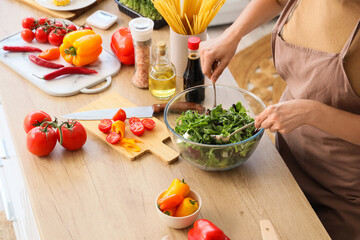 Young woman making vegetable salad in kitchen