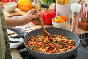 Young woman frying rice with vegetables in kitchen, closeup
