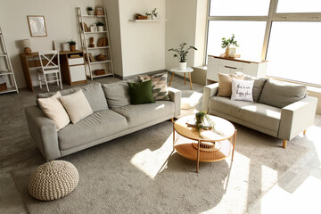 Interior of light living room with grey sofas, tables and shelf unit
