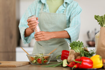 Young woman salting vegetable salad in kitchen, closeup