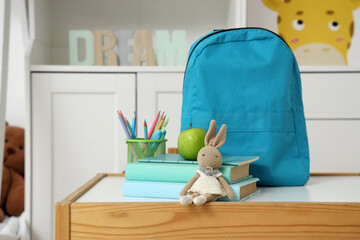 Blue backpack with toy, apple and books on table in children's room