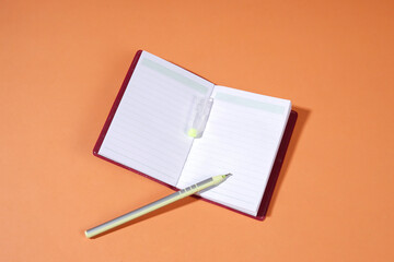 A yellow ballpoint pen and a red book rest on an orange background