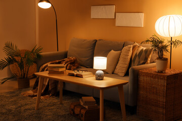 Interior of dark living room with glowing lamps, sofa and table at night